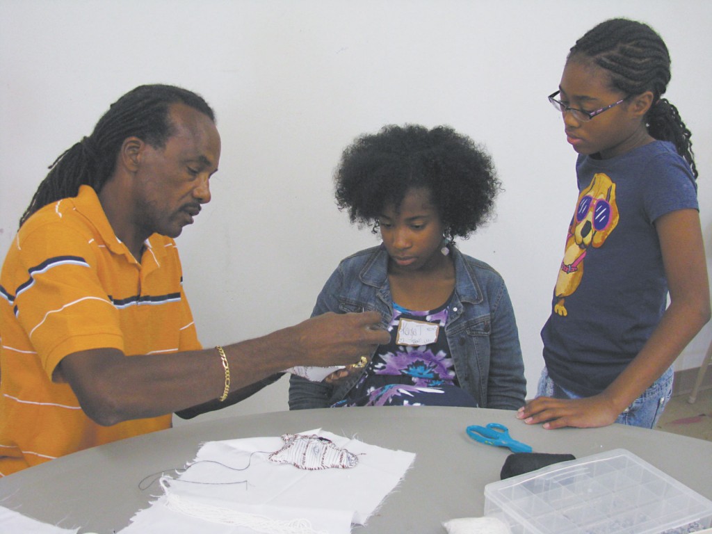 Big Chief Darryl Montana demonstrates the art of beading of Mardi Gras Indian costumes for Kayla Tiffith and Bria Johnson.